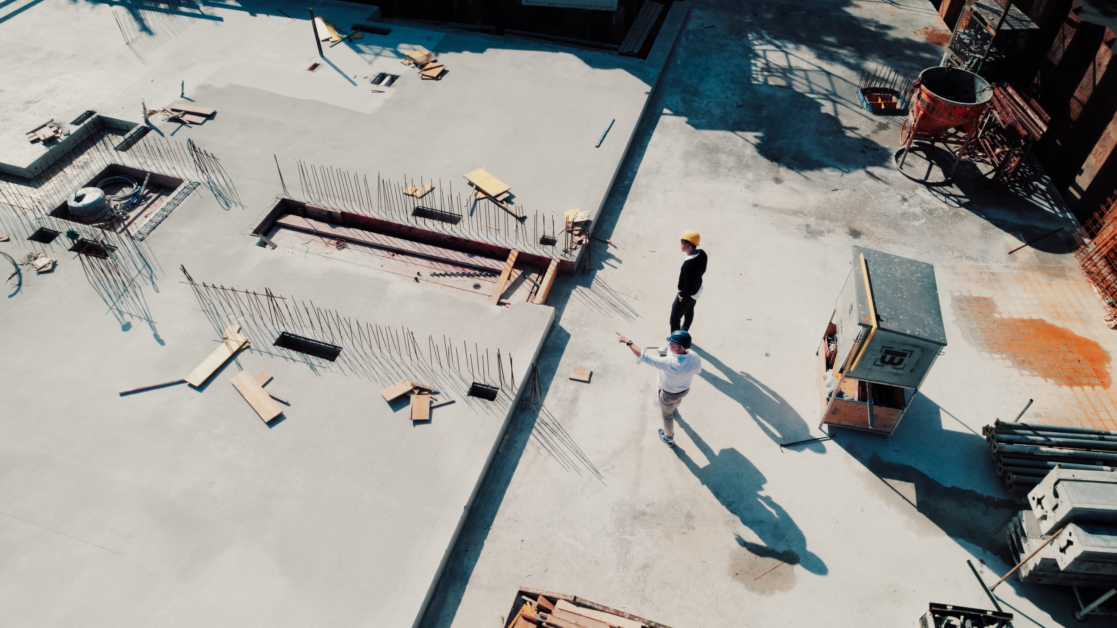 Luftaufnahme einer Baustelle: Rohbau-Decke mit Bewehrungsstahl; zwei Personen mit Bauhelmen besprechen die Arbeiten